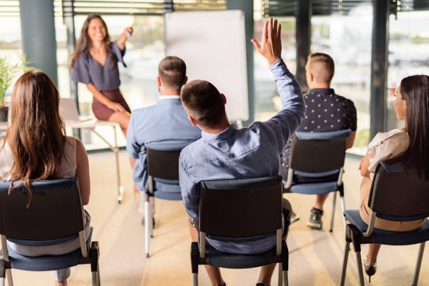 CEO giving a business presentation to group of her colleagues in a board room while aiming at one person who wants to ask something